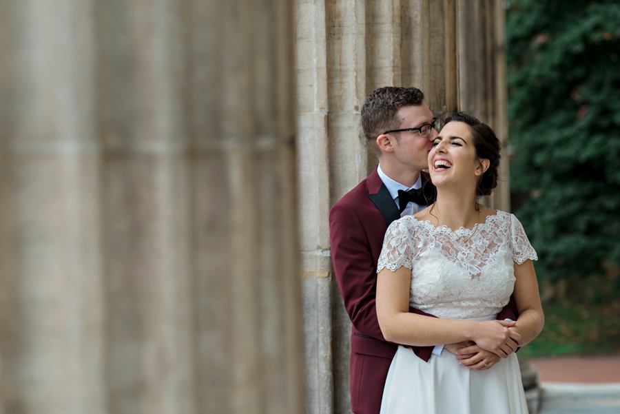 A bride laughs as her groom whispers into her ear.